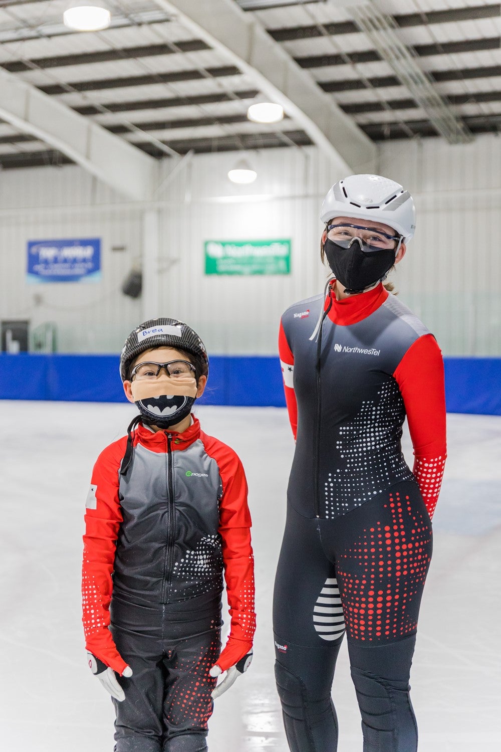 Brea and Akutaq stand side by side on the ice in their speed skating uniforms