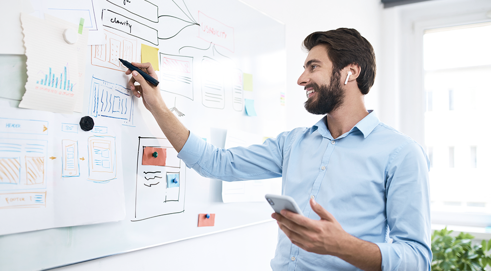 man working on a whiteboard with creative elements posted on it