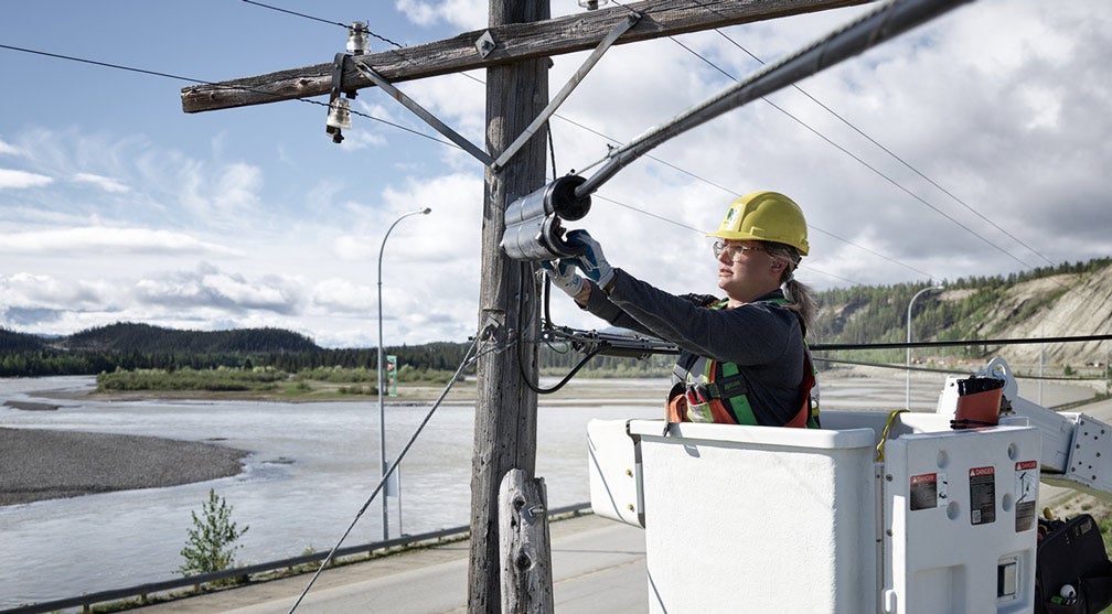 Female technician working on a pole with a northern landscape as a background