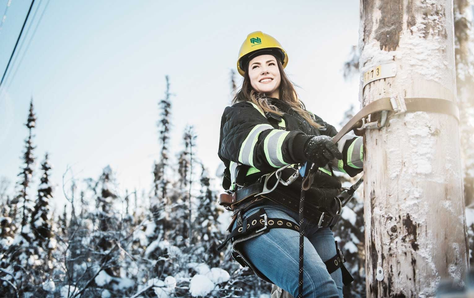 Service technician Nicole climbing a pole in a snowed northern background