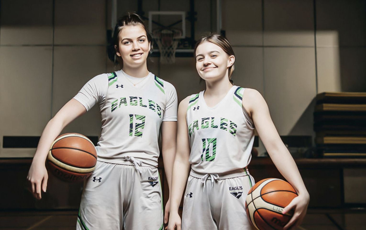 Lilly and Grace stand on the court, basketball in their hands, smiling brightly.